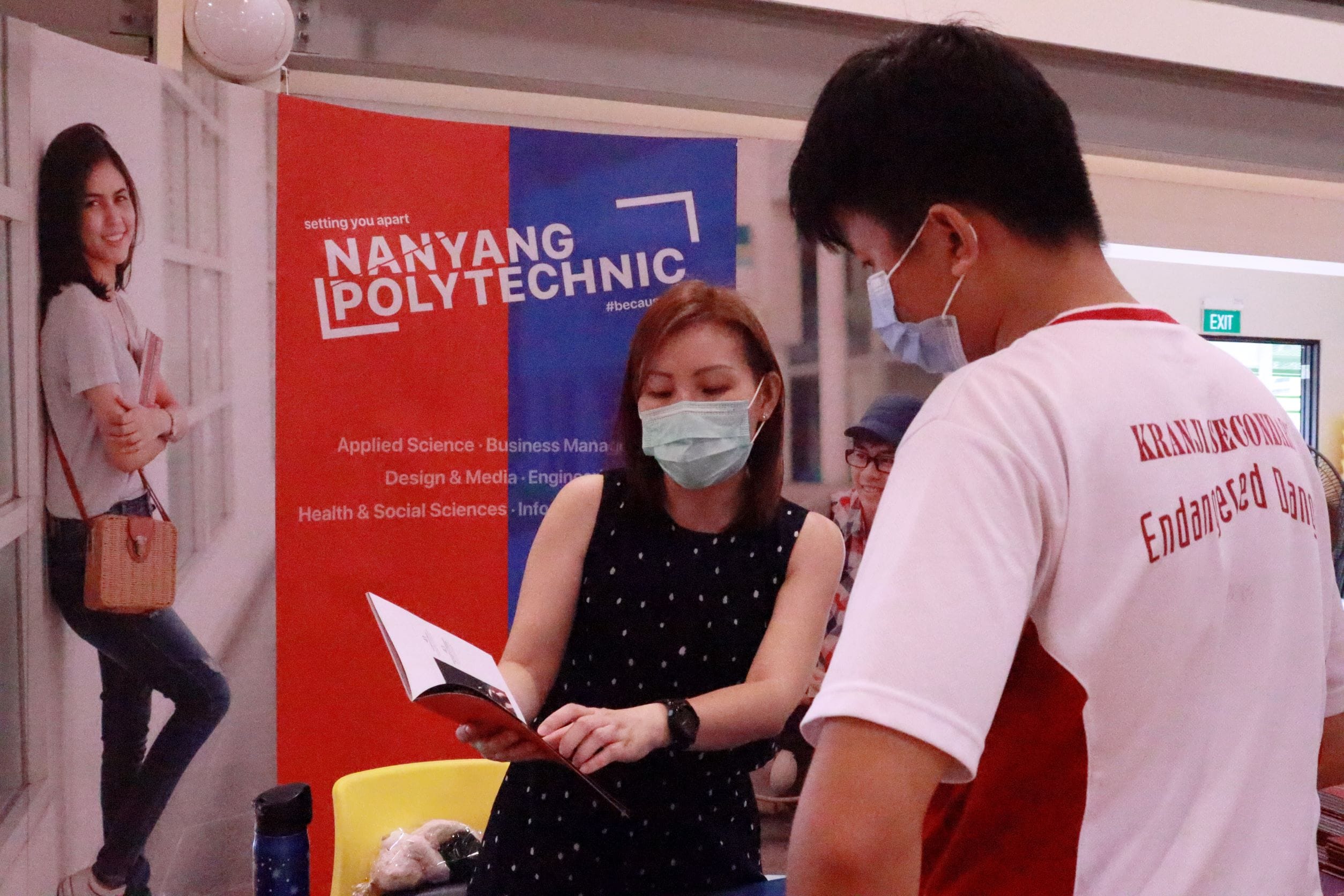 Two masked people review a brochure at a Nanyang Polytechnic booth during an education fair.